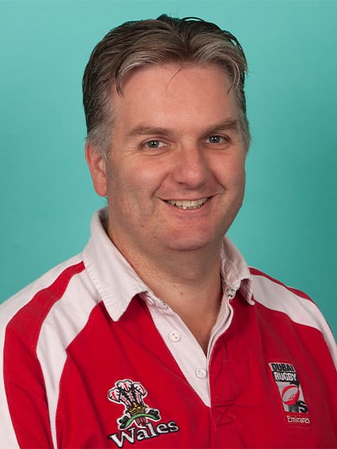 headshot of Graham in red t-shirt with teal coloured background